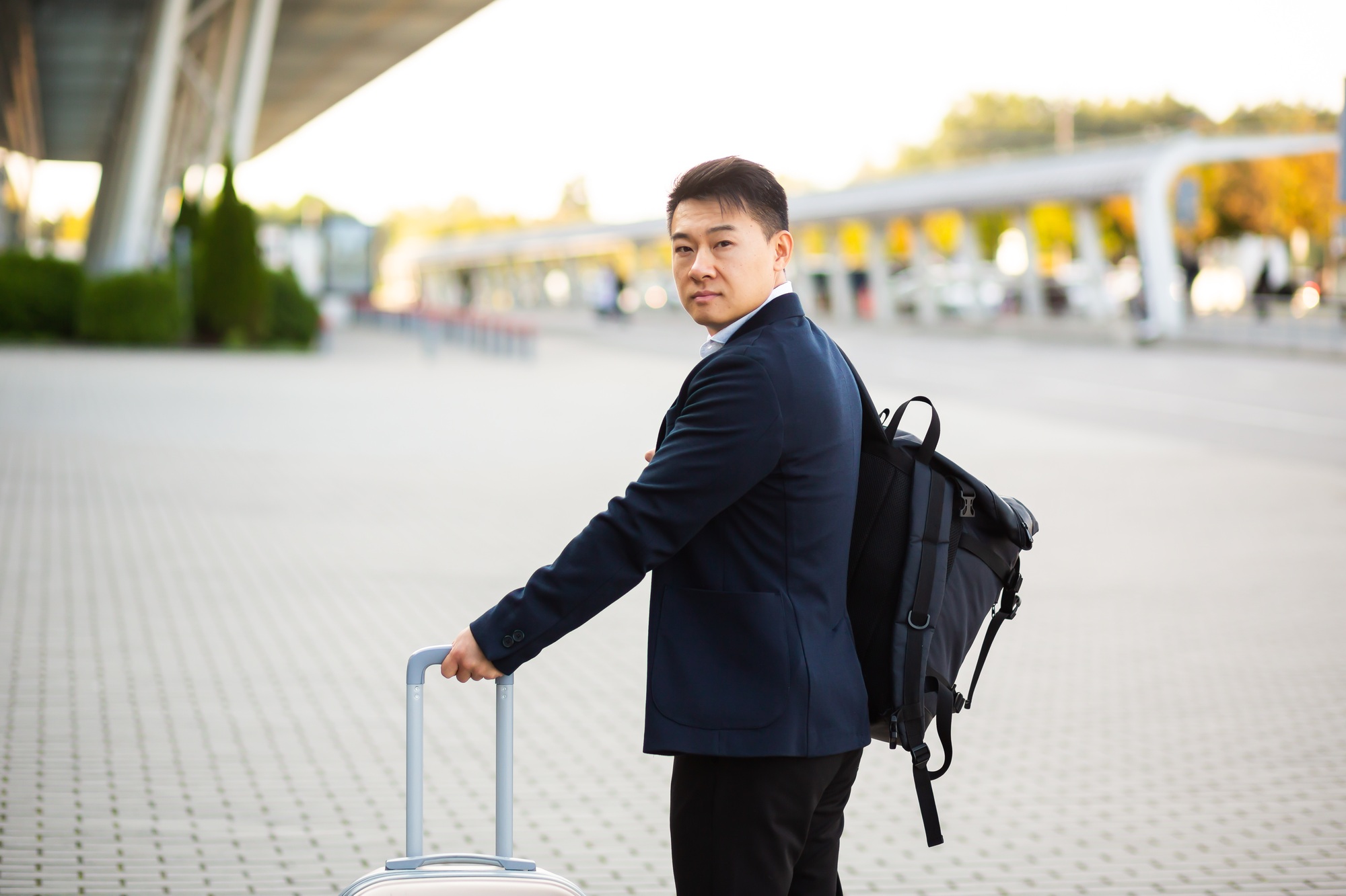 Successful asian businessman near airport and bus station goes with suitcases serious